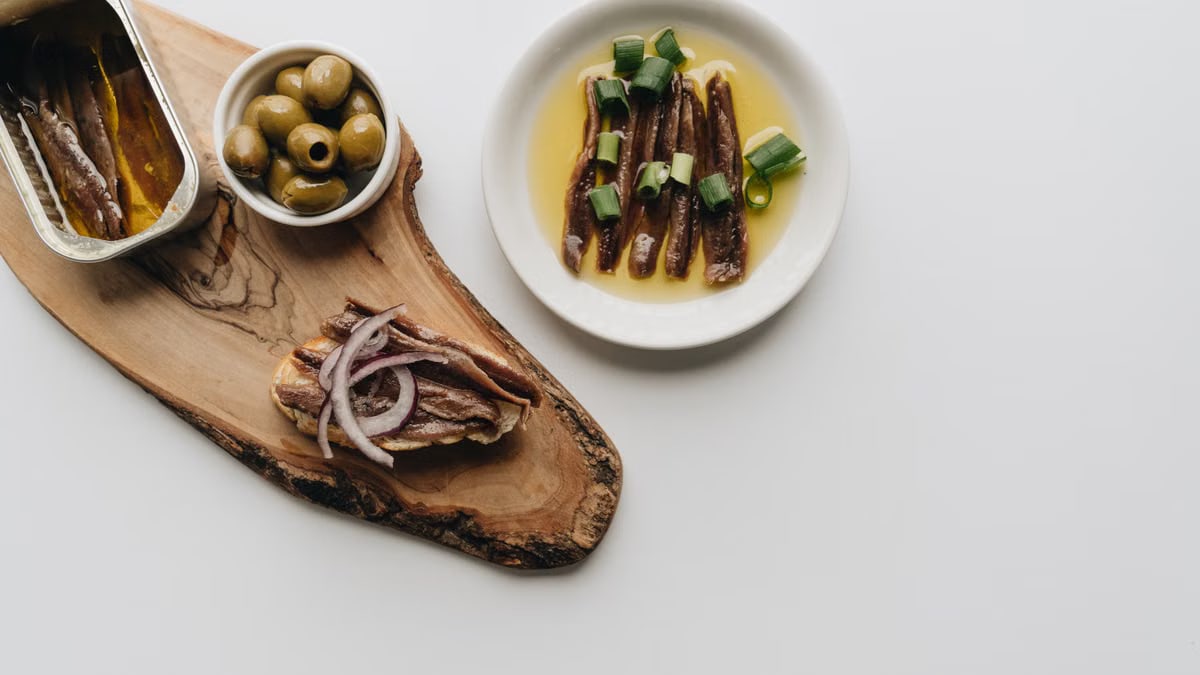 Delicious arrangement of anchovies and olives on a wooden board. Perfect food photography for culinary topics.