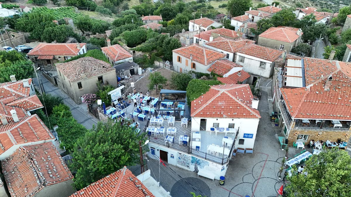 Explore a serene village in Gökçeada, Türkiye with charming red-tiled roofs and outdoor dining spaces.