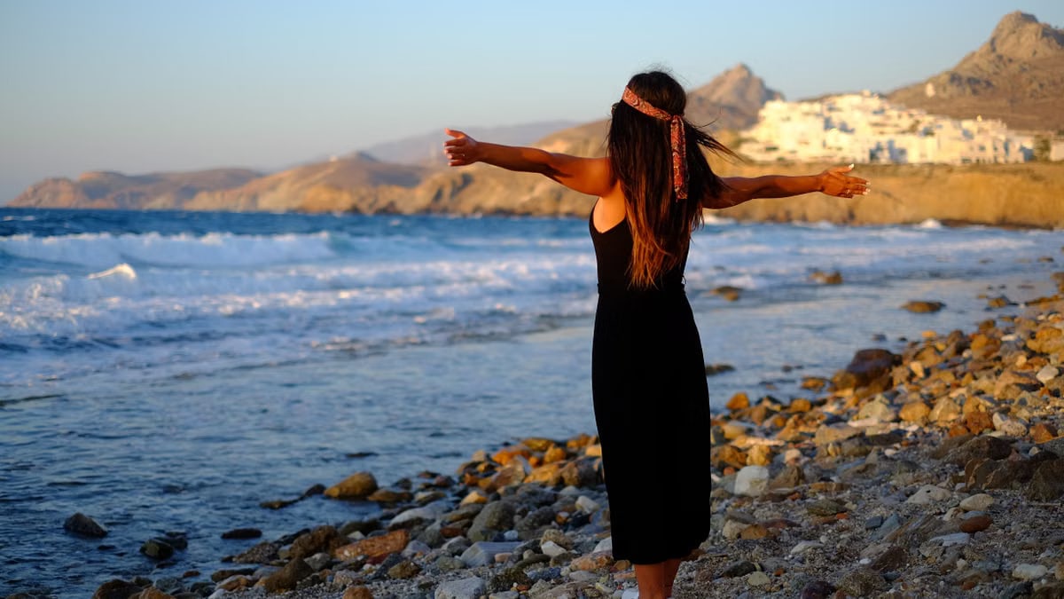 Woman enjoying freedom at sunset on a rocky beach in Greece.